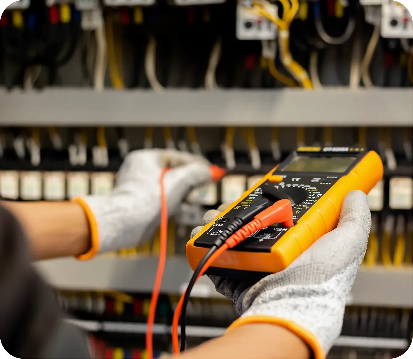 Electrician testing wires in electrical panel with a multimeter, wearing gloves.