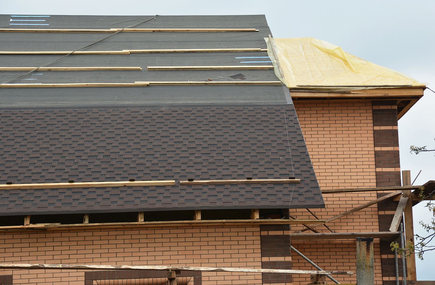 Roof under construction on a brick building, with dark shingles and exposed yellow underlayment. Roof under construction on a brick building, with dark shingles and exposed yellow underlayment.