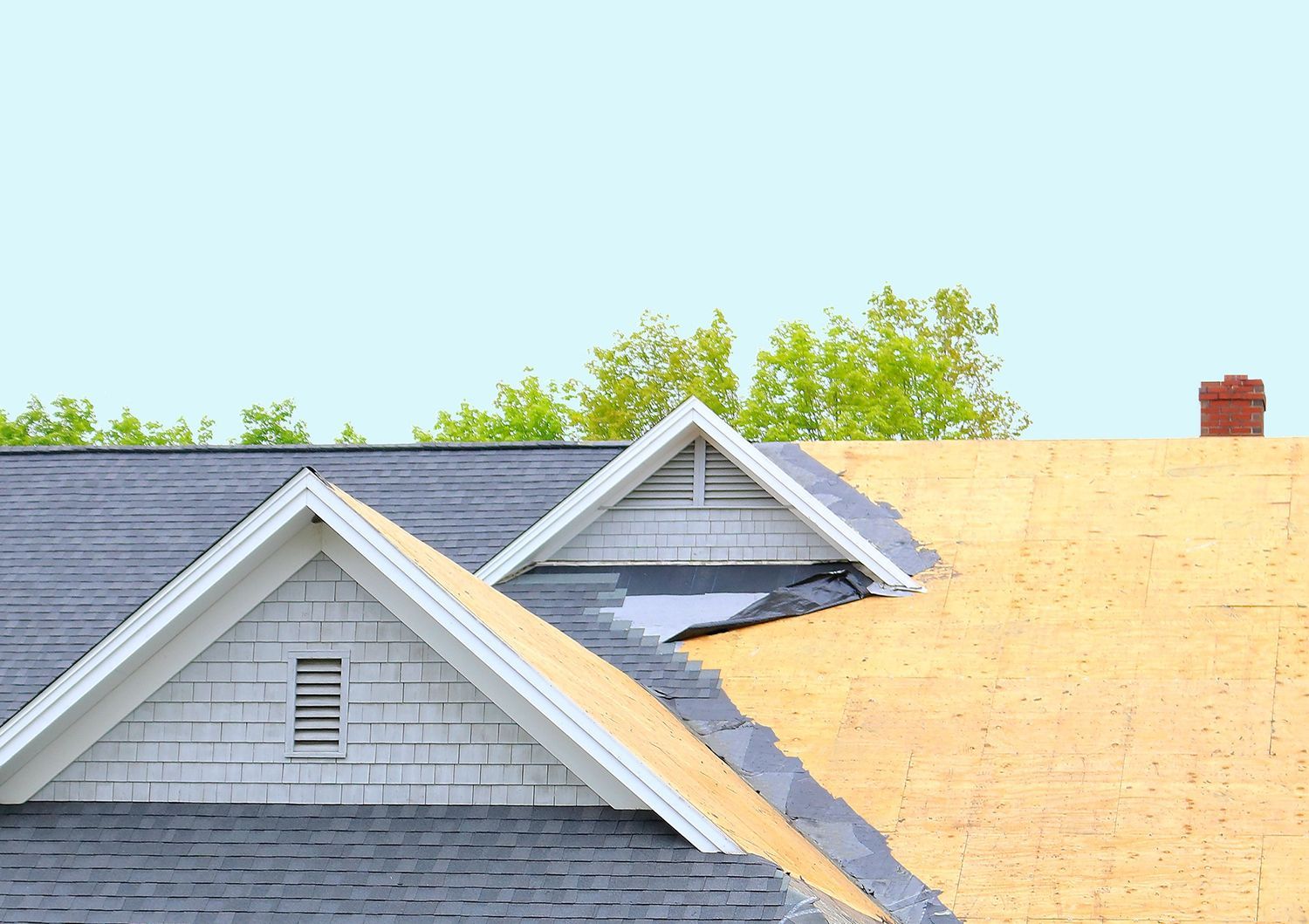 Roofing work on a gray house, with a partially covered roof and blue sky above. Roofing work on a gray house, with a partially covered roof and blue sky above.