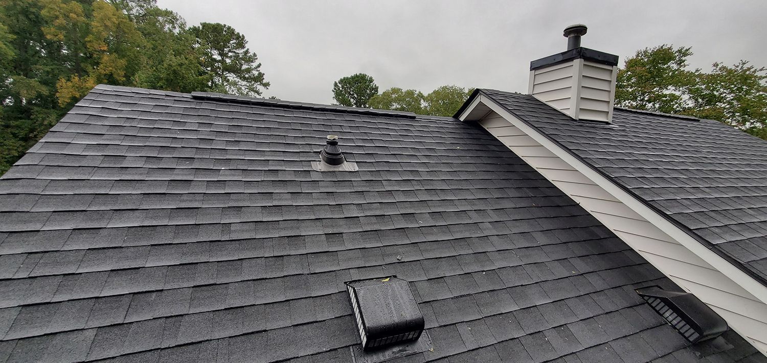 Gray shingled roof with two vents and a chimney under cloudy skies Gray shingled roof with two vents and a chimney under cloudy skies