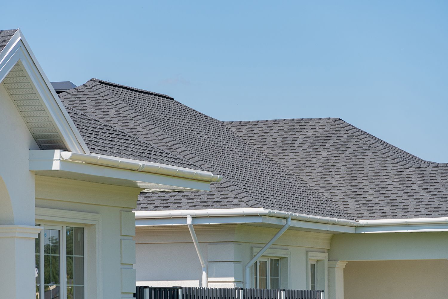 Suburban house roof with gray shingles and white trim under a clear blue sky Suburban house roof with gray shingles and white trim under a clear blue sky