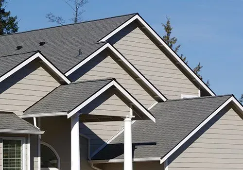 Suburban house rooflines with gray shingles and beige siding under a blue sky Suburban house rooflines with gray shingles and beige siding under a blue sky
