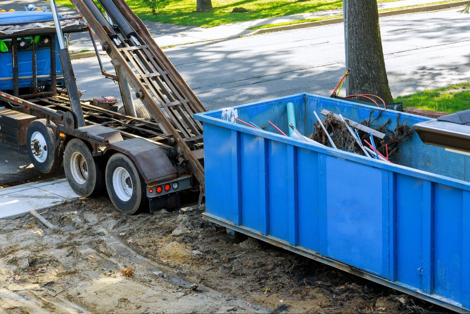A large blue roll-off dumpster being loaded onto a truck on a residential street.