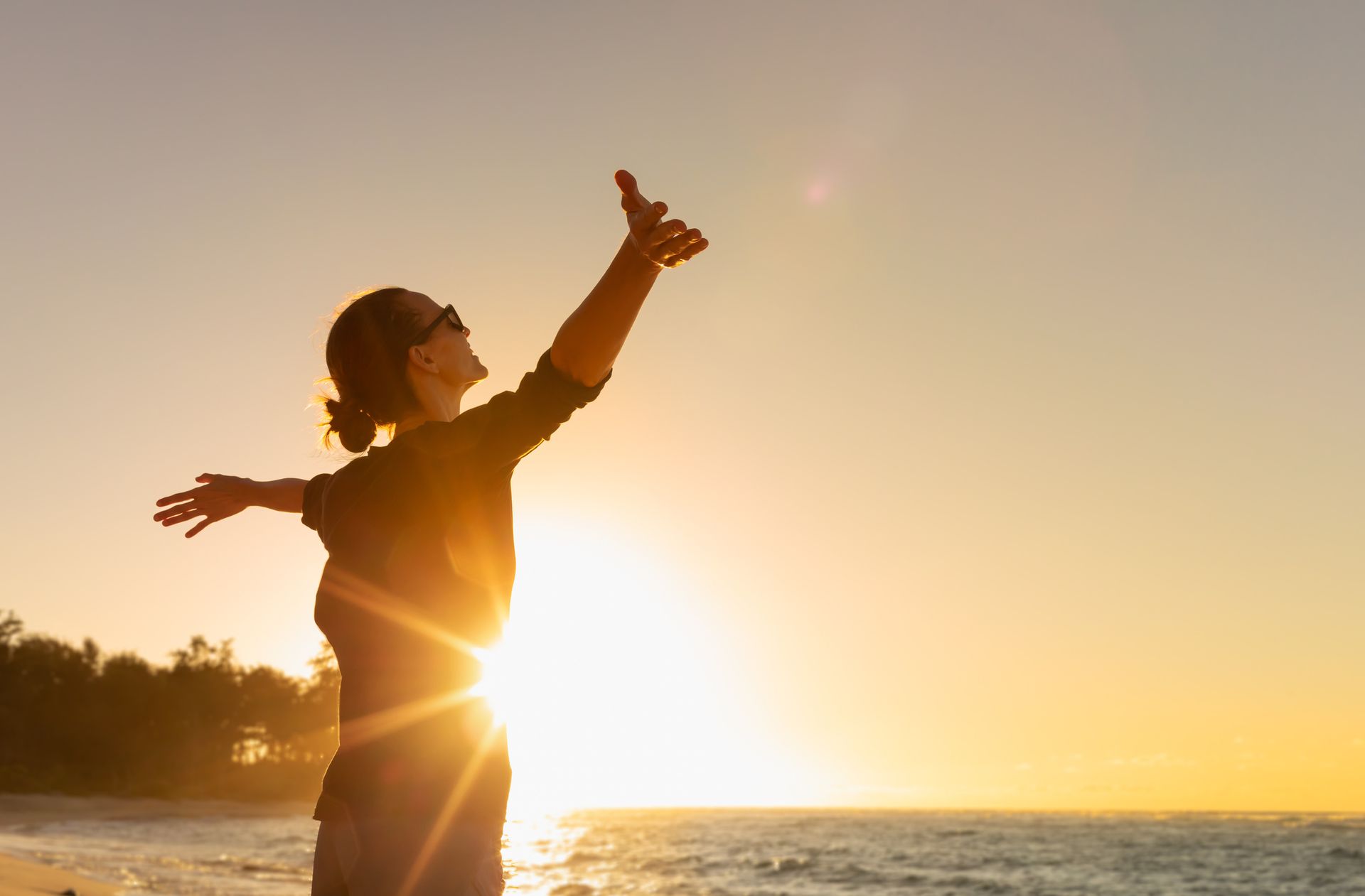 A woman is standing on the beach with her arms outstretched at sunset.