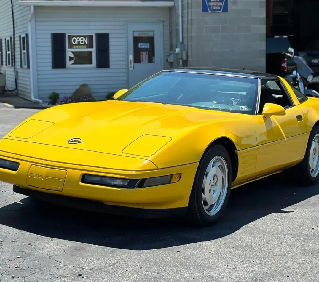 A yellow corvette is parked in front of a garage.