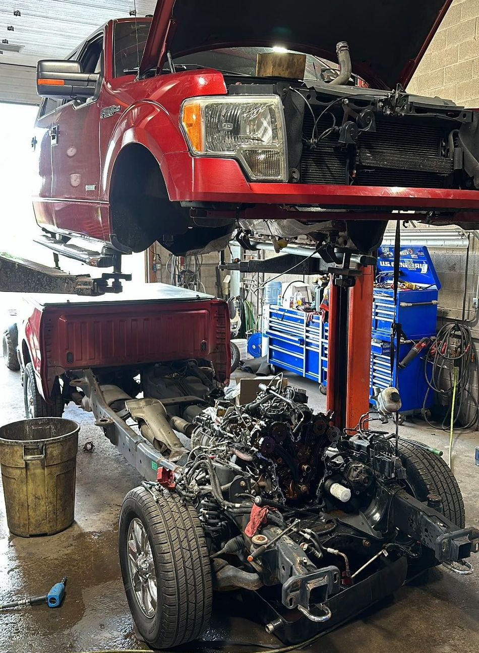 A red truck with the hood up is being worked on in a garage.