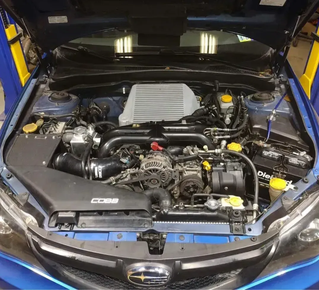 The engine of a blue Subaru is shown with the hood open.