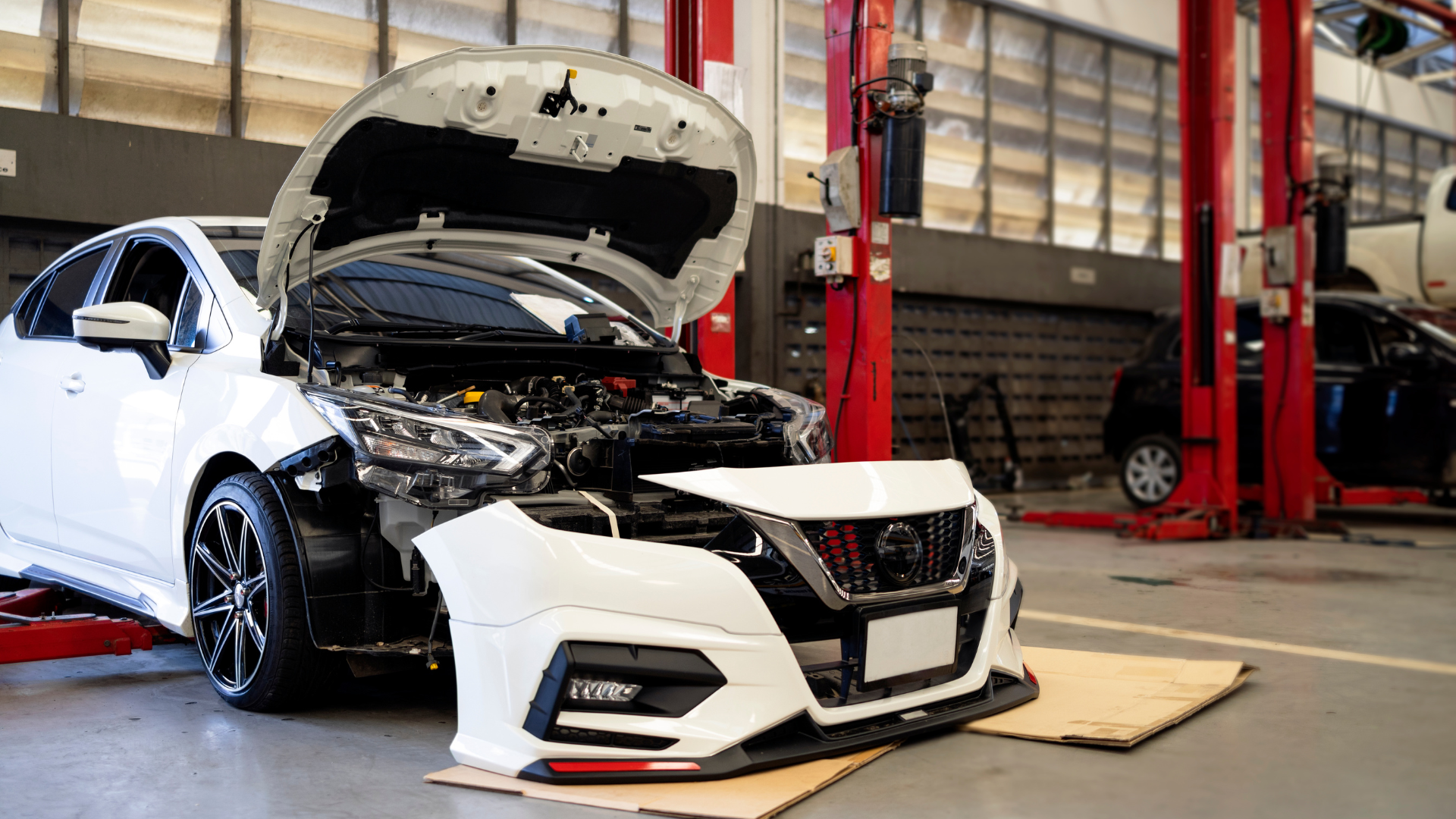 A white car is being repaired in a garage with the hood open.