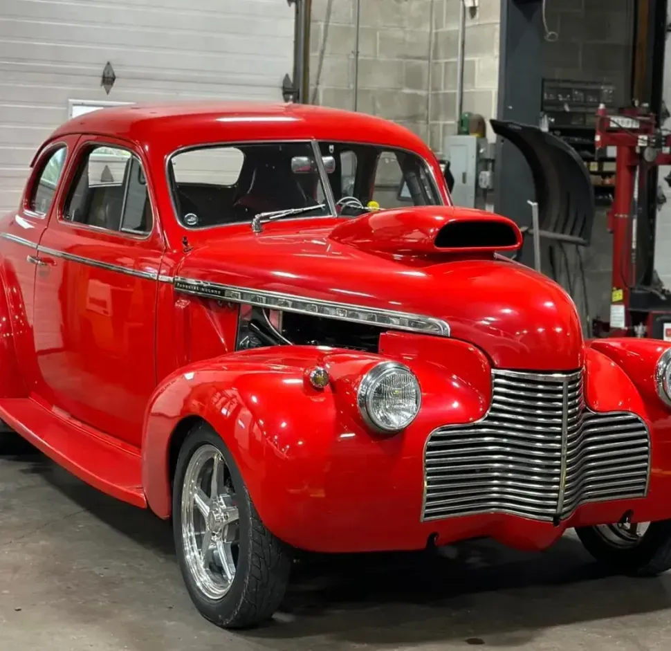 A red car with the hood up is parked in a garage.