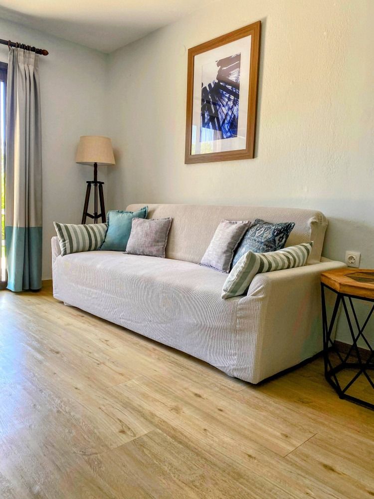 A living room with a couch , table , lamp and picture on the wall.
