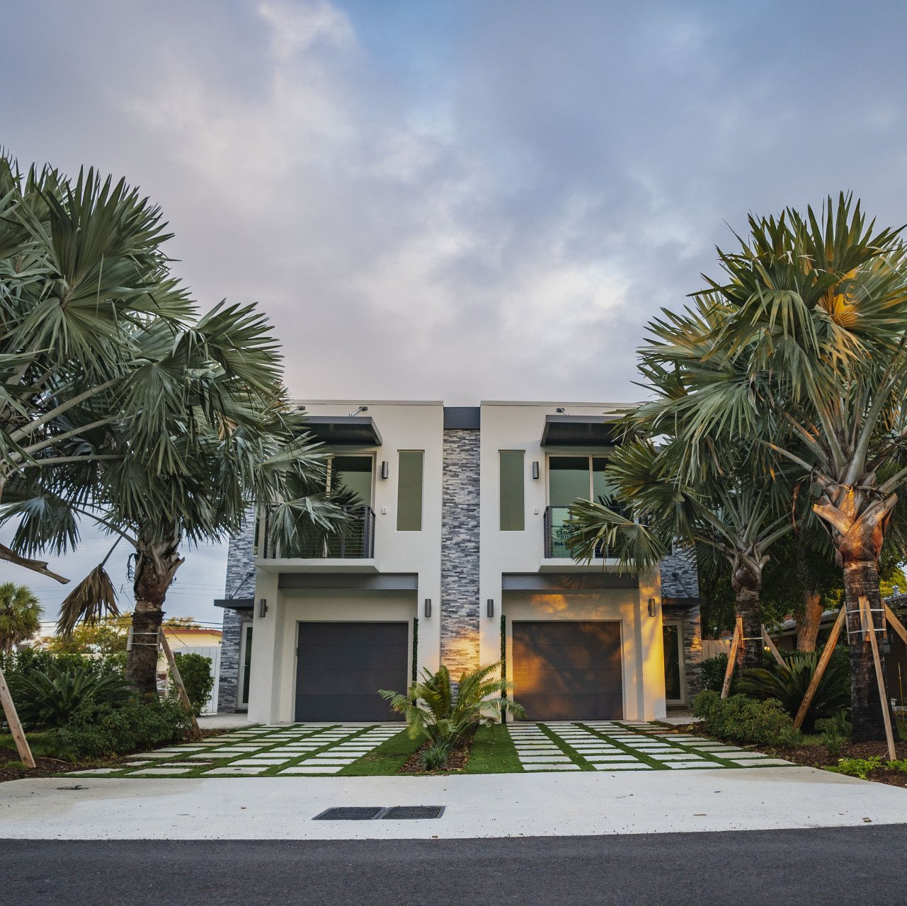 a house with two garages and palm trees in front of it