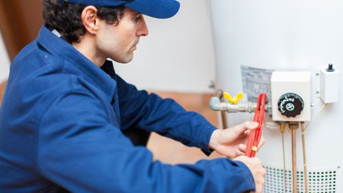 Person working on a hot water heater, adjusting wires near the gas valve in a utility room.