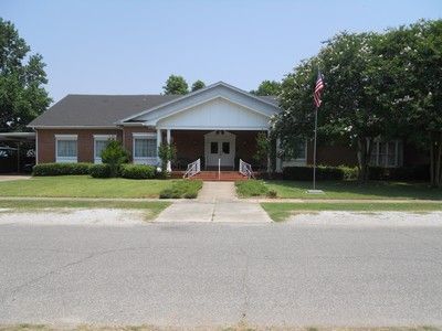 Brick building with white trim, a covered entrance, and American flag on a sunny day.
