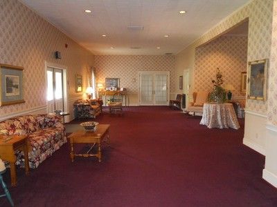 Empty funeral home waiting area with red carpet, floral furniture, and patterned wallpaper.