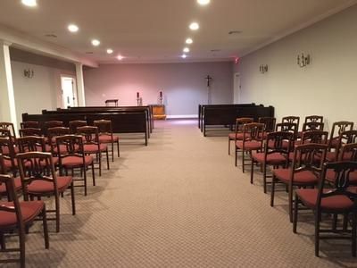 Funeral home chapel with rows of chairs facing a wooden altar and podium on a raised platform.