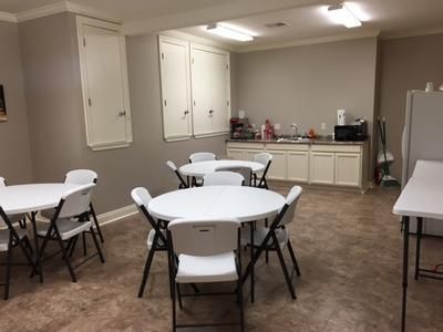 A break room with round white tables and chairs, cabinets, sink, and microwave.