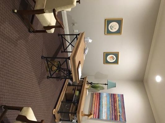 An office setting with a desk, chairs, artwork, and a lamp on a side table.