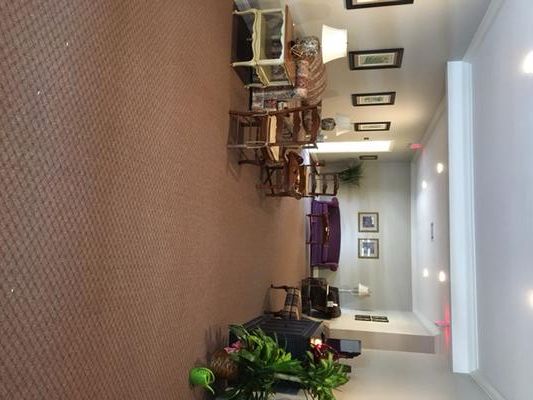 A hallway with brown carpet, several seating areas, artwork on walls, and overhead lighting.