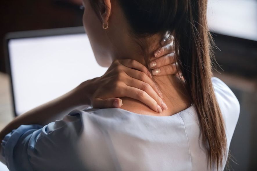 A woman is holding her neck in pain while sitting in front of a computer.