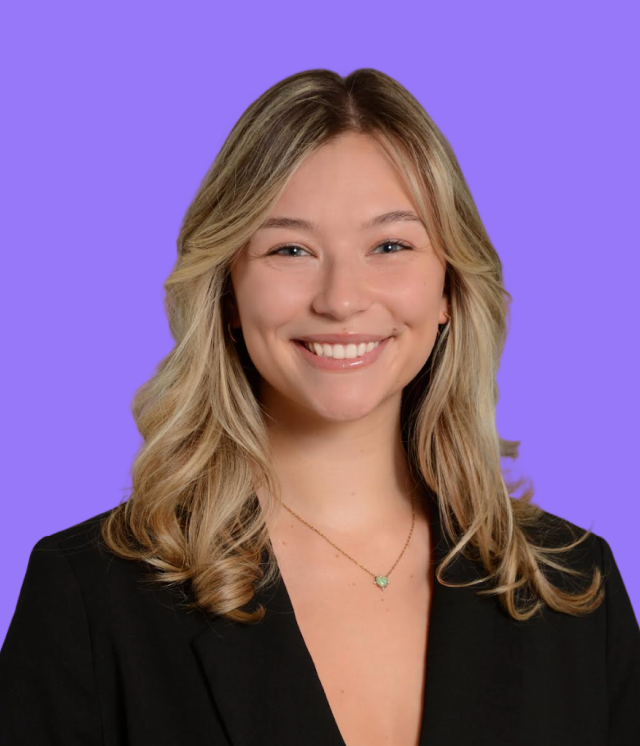 A woman wearing a black shirt and a necklace is smiling against a purple background.