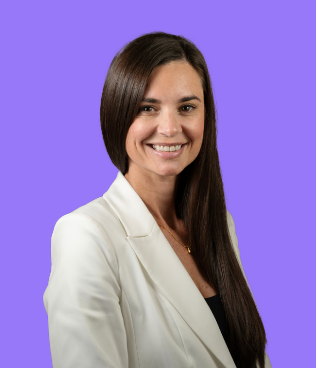 A woman in a white jacket is smiling in front of a purple background
