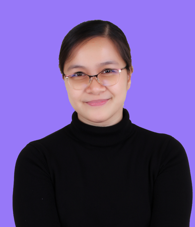 A woman wearing glasses and a blue shirt is standing in front of a purple background.