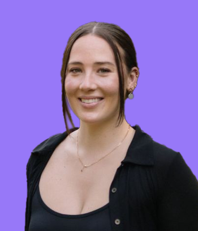 A woman wearing a black shirt and a necklace is smiling against a purple background.
