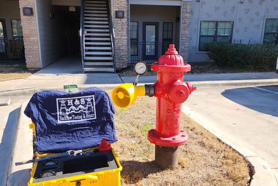 A man is working on a red fire hydrant in a parking lot.
