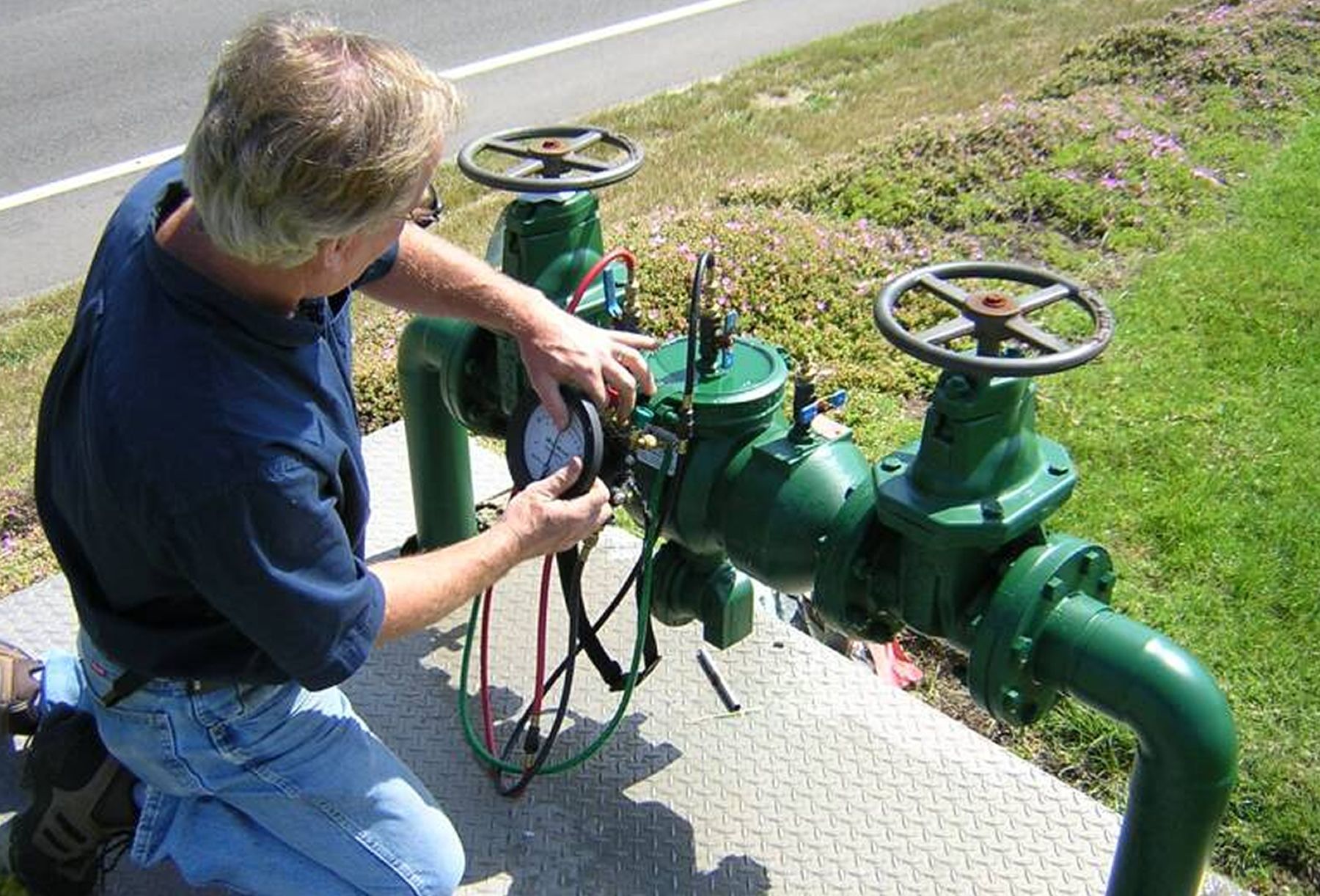 A man is working on a green pipe with a gauge on it