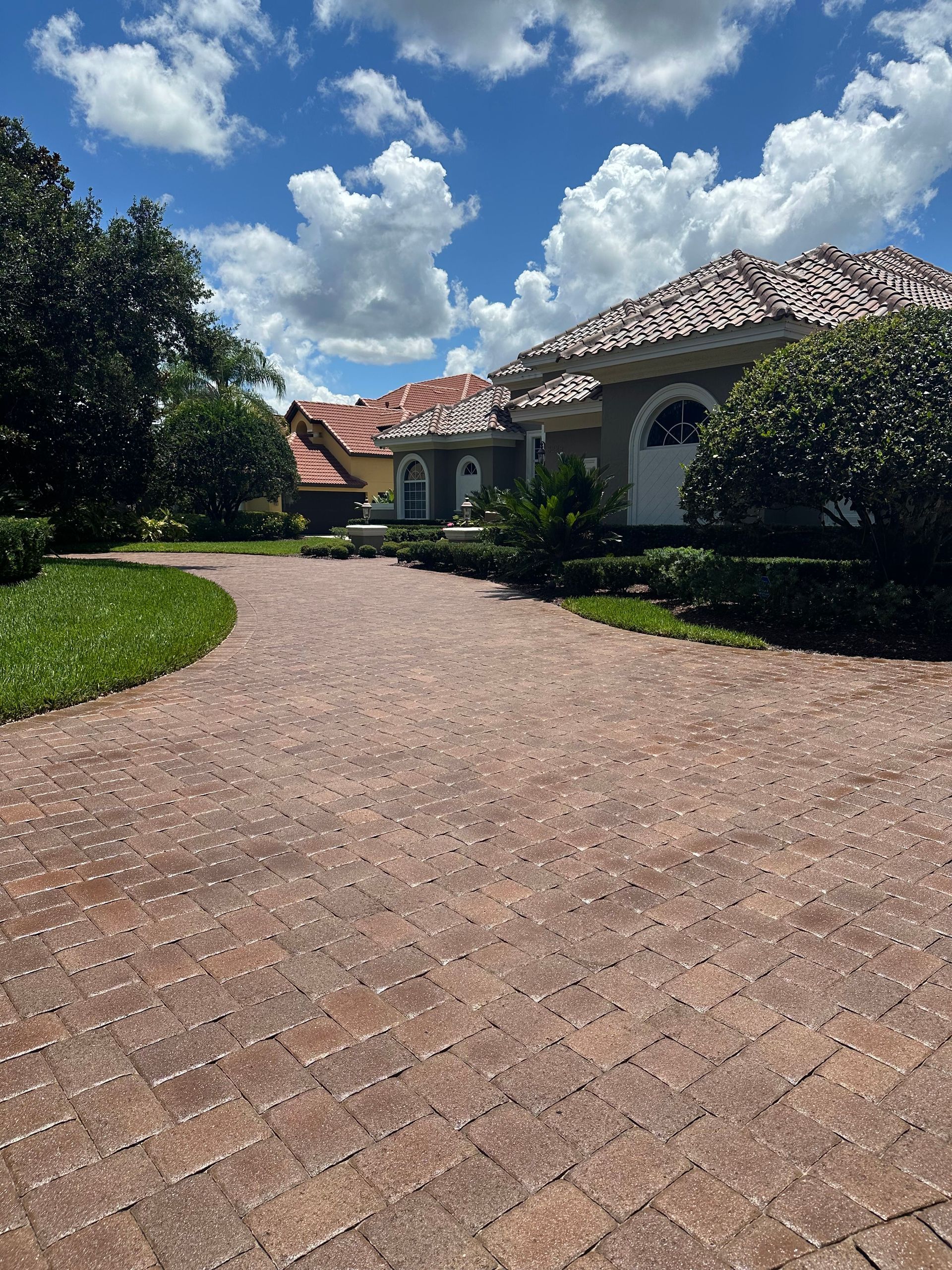 A brick driveway leading to a large house on a sunny day