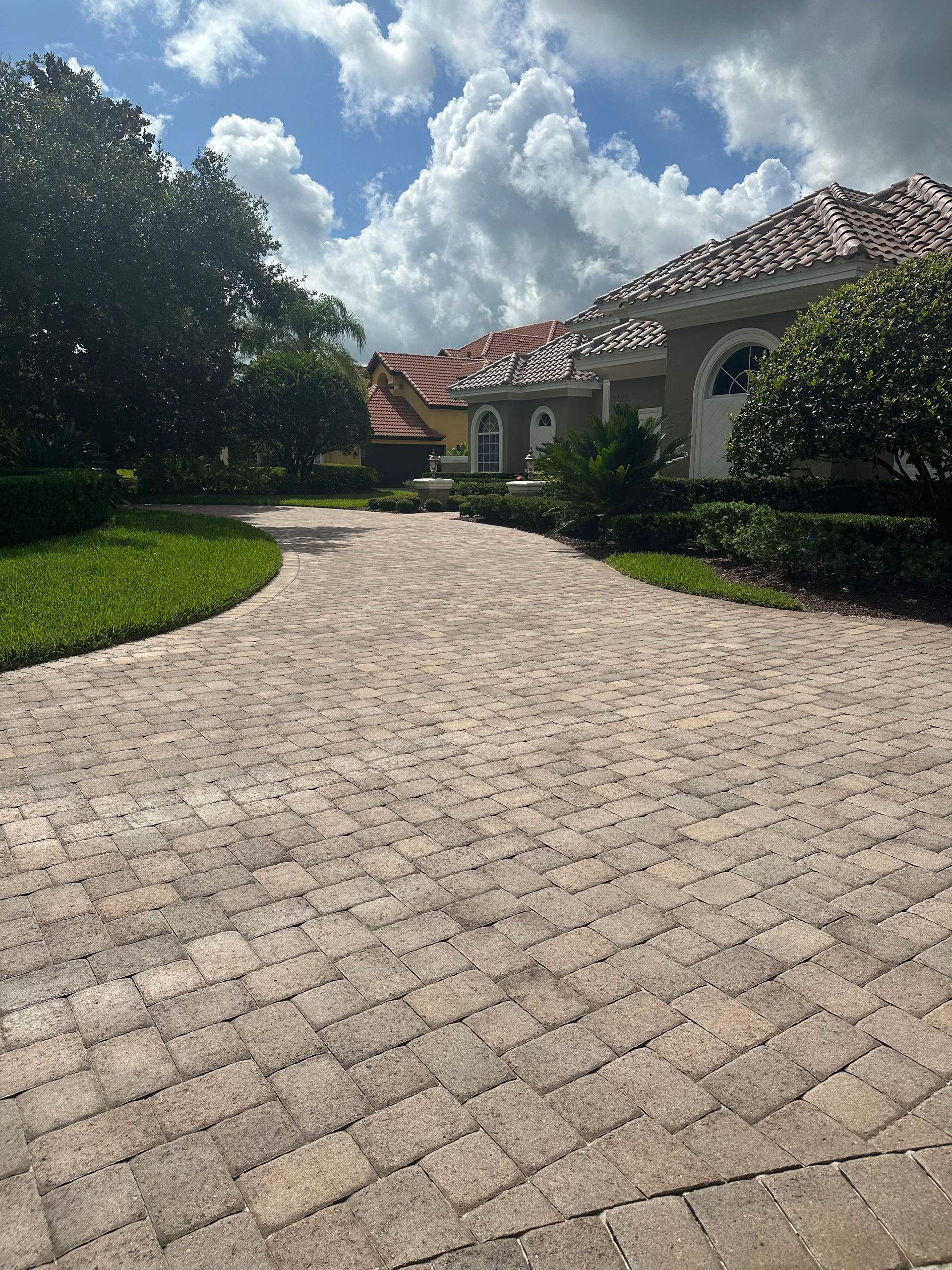 A brick driveway leading to a large house on a sunny day.