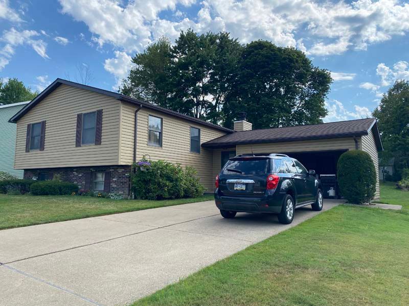 Tan house with a black SUV in the driveway on a sunny day.