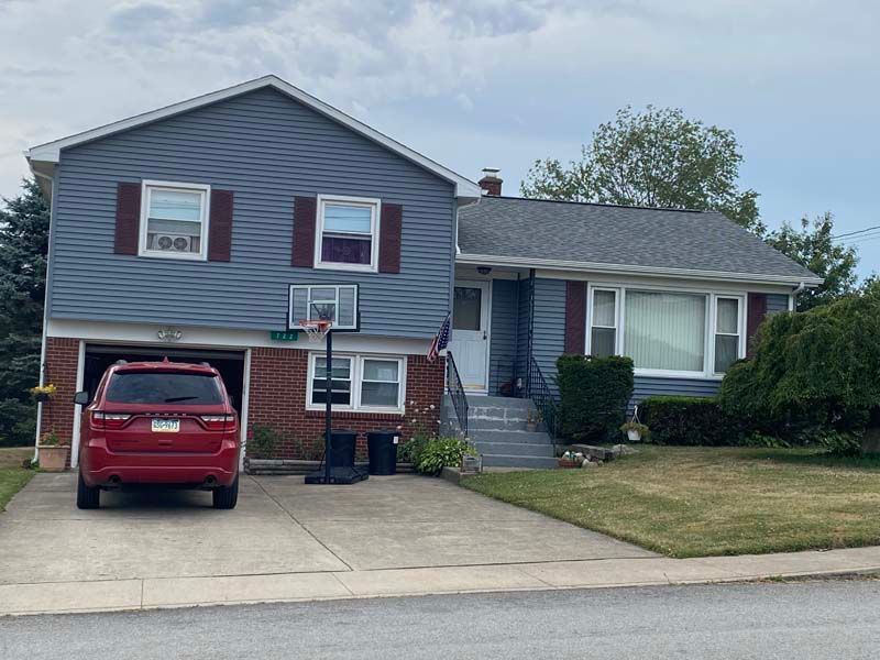 Two-story blue house with red car in garage, basketball hoop, and manicured lawn.