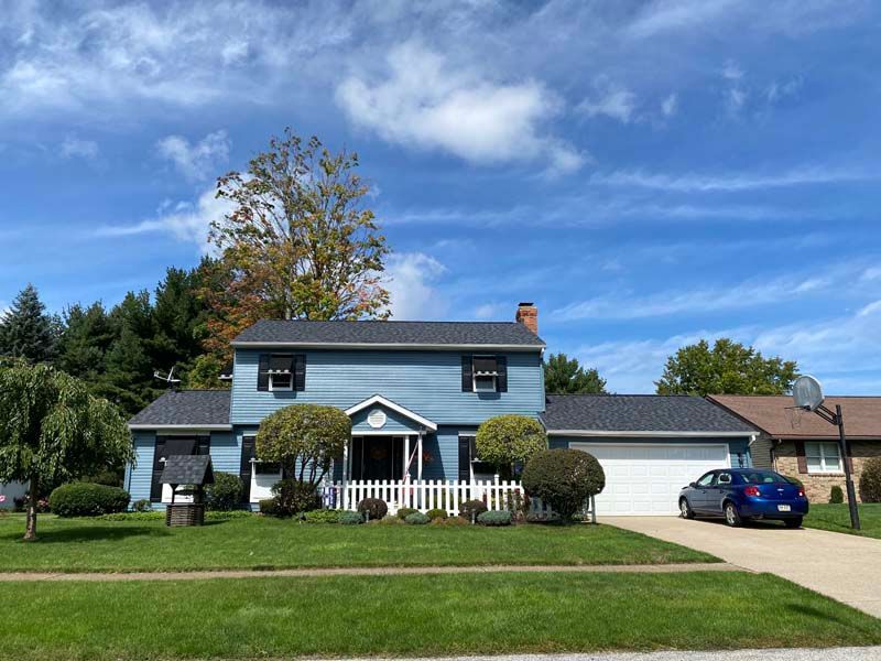Blue two-story house with white garage, driveway, and lawn on a sunny day. Blue car parked in the driveway.