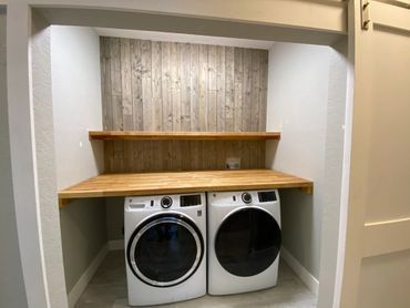 A washer and dryer are sitting under a wooden table in a laundry room. A washer and dryer are sitting under a wooden table in a laundry room.