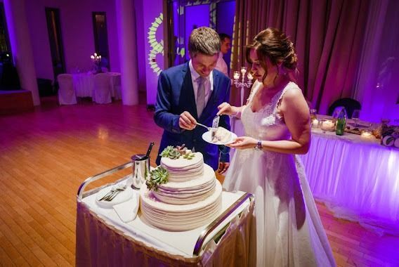 Bride and groom cutting wedding cake at reception, with violet lighting.