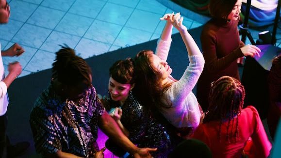 People dancing in a club with blue and purple lighting; one woman with arms raised.