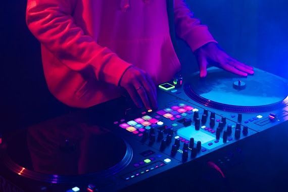 DJ at work, illuminated by blue and pink lights, using turntables and mixer.