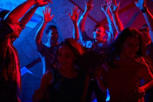 People dancing with hands raised in a club with red and blue lights.