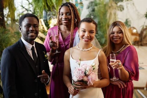 Wedding group: Bride in white dress, three people with champagne; smiles indoors.