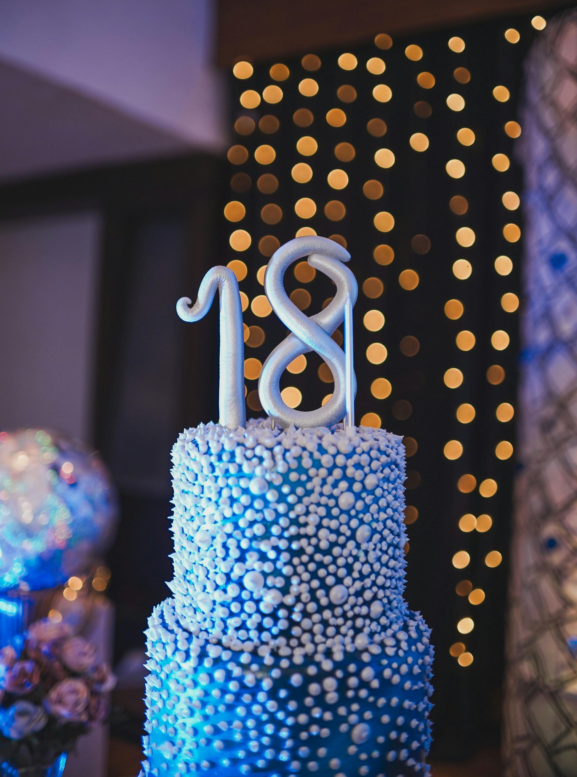 Blue tiered cake with white pearl-like frosting, topped with a silver 
