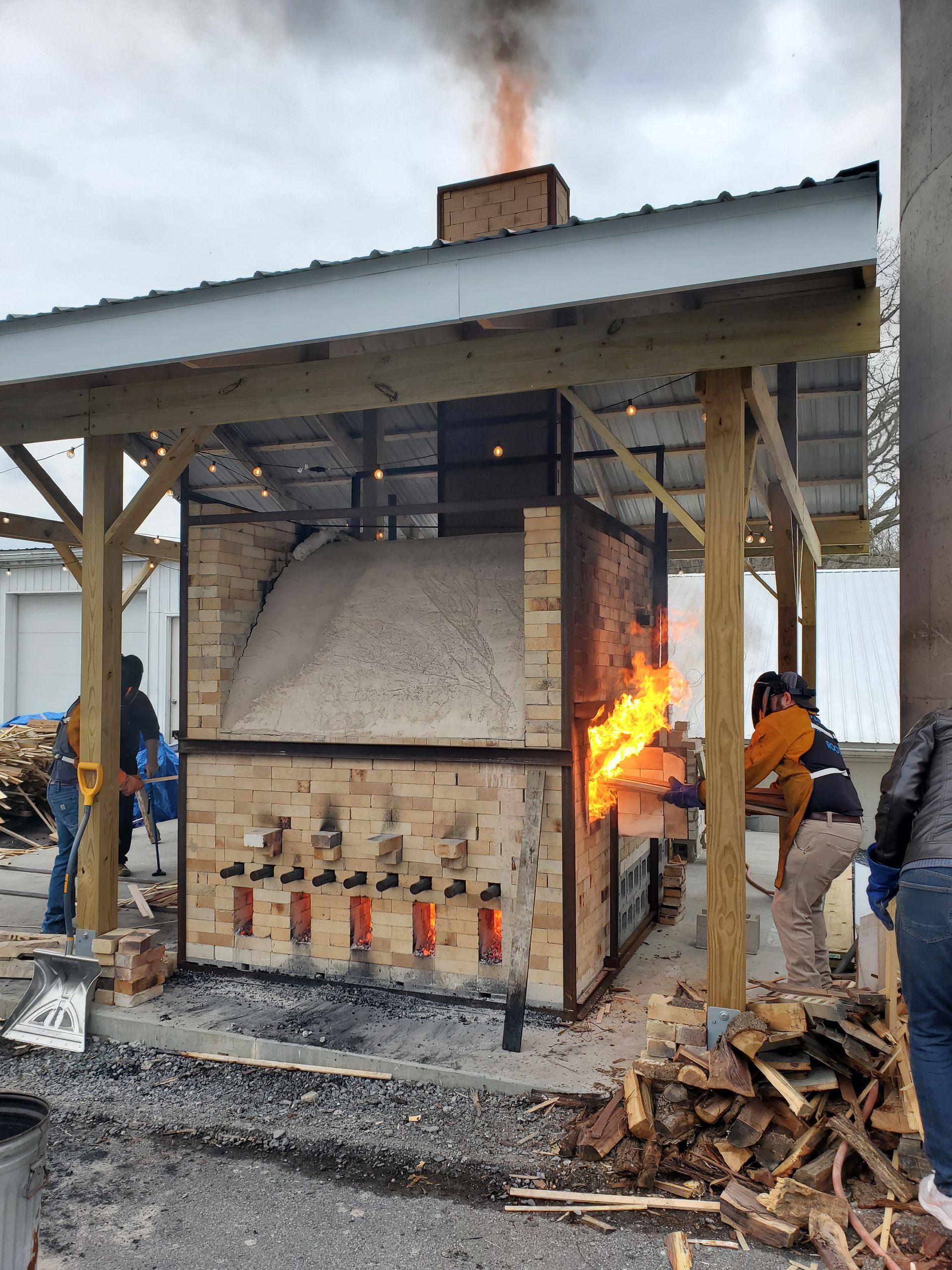 A group of people are standing around a large brick oven with flames coming out of it.