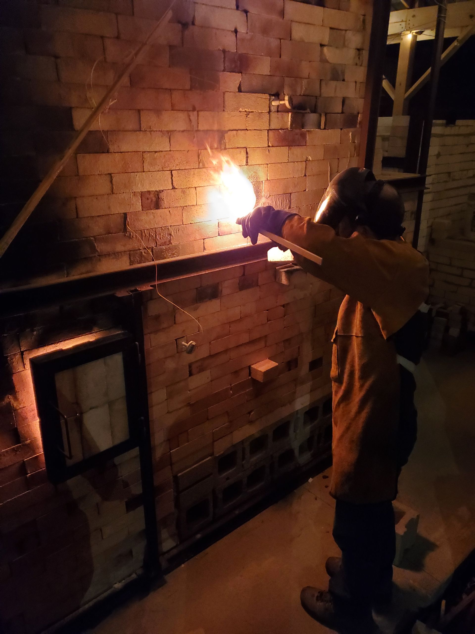 A man wearing a welding helmet is working on a brick wall