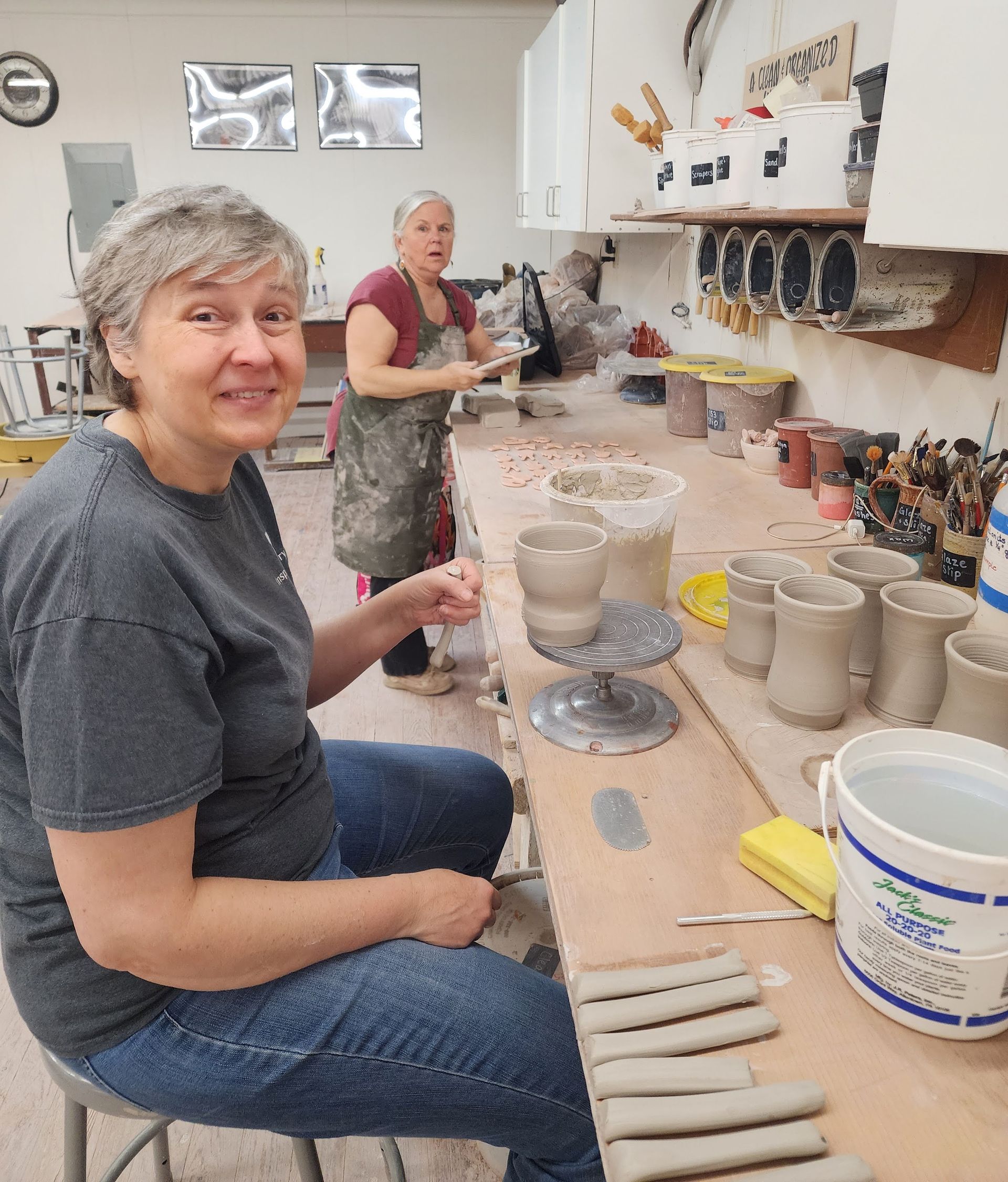 A woman is sitting at a table in a pottery studio
