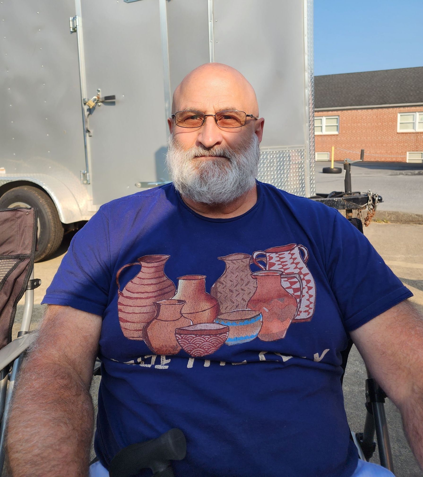 A bald man with a beard is sitting in a wheelchair wearing a blue shirt with vases on it