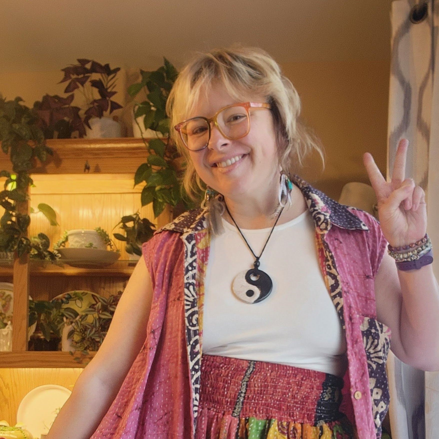 A woman wearing glasses and a yin yang necklace giving a peace sign