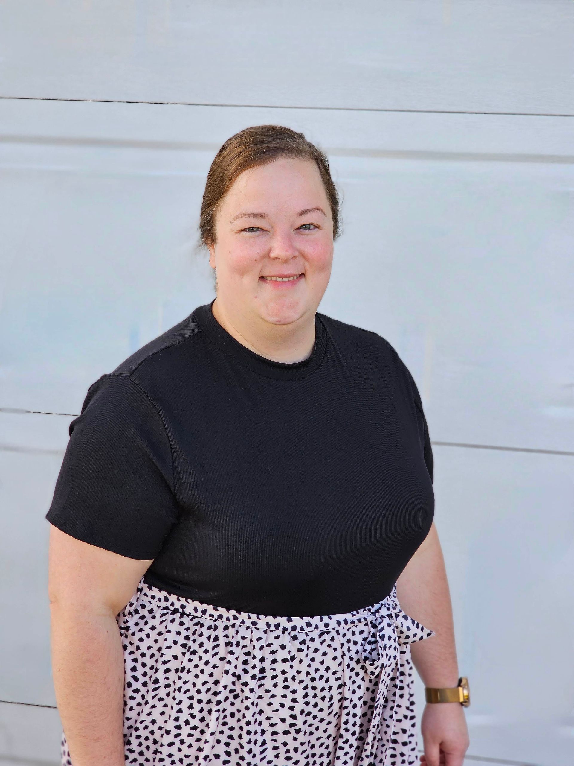 A woman wearing a black shirt and a leopard print skirt is standing in front of a garage door.