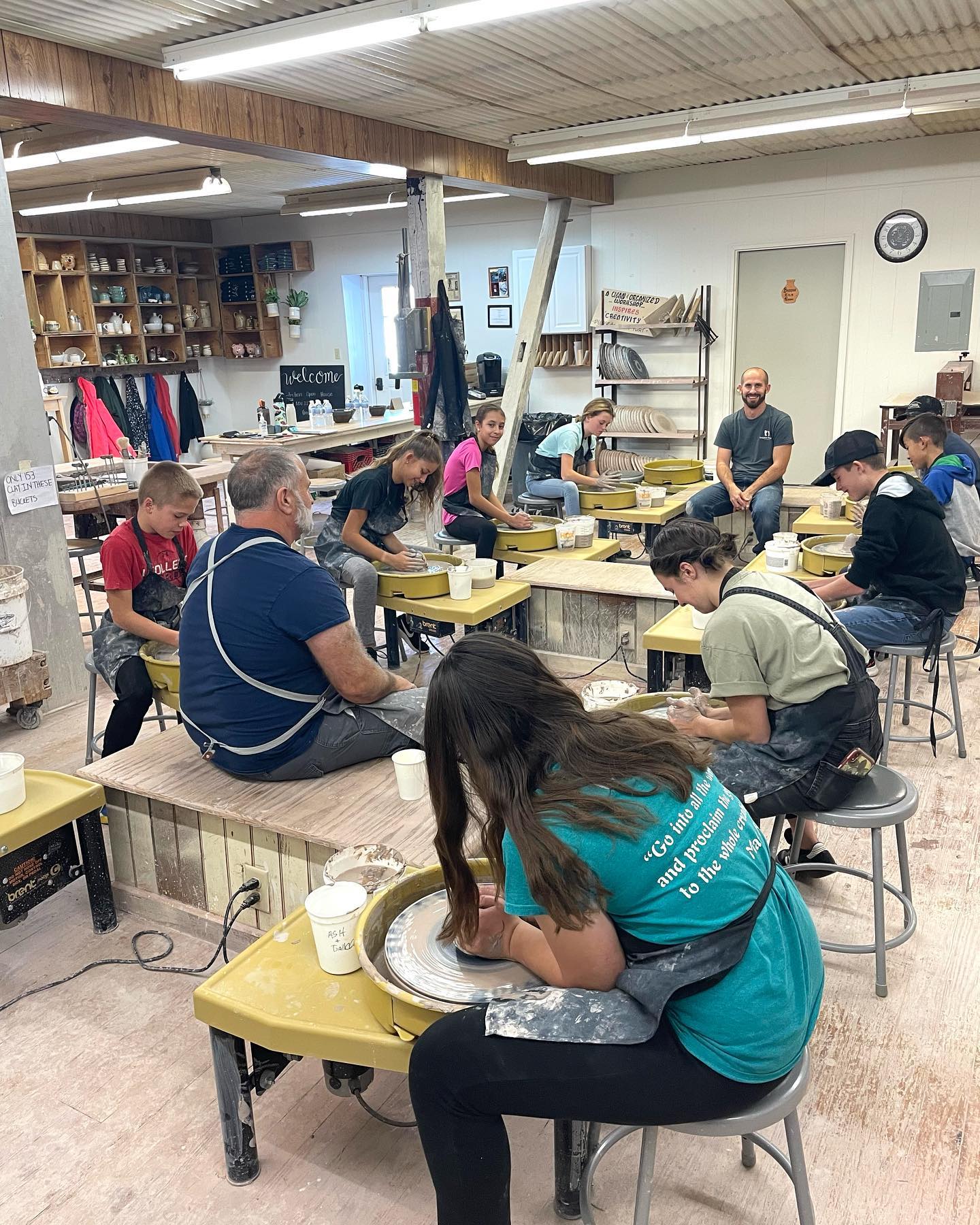 A group of people are working on pottery wheels in a pottery studio.
