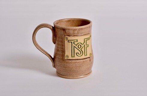 a brown mug with the letters tsf on it is sitting on a white surface .
