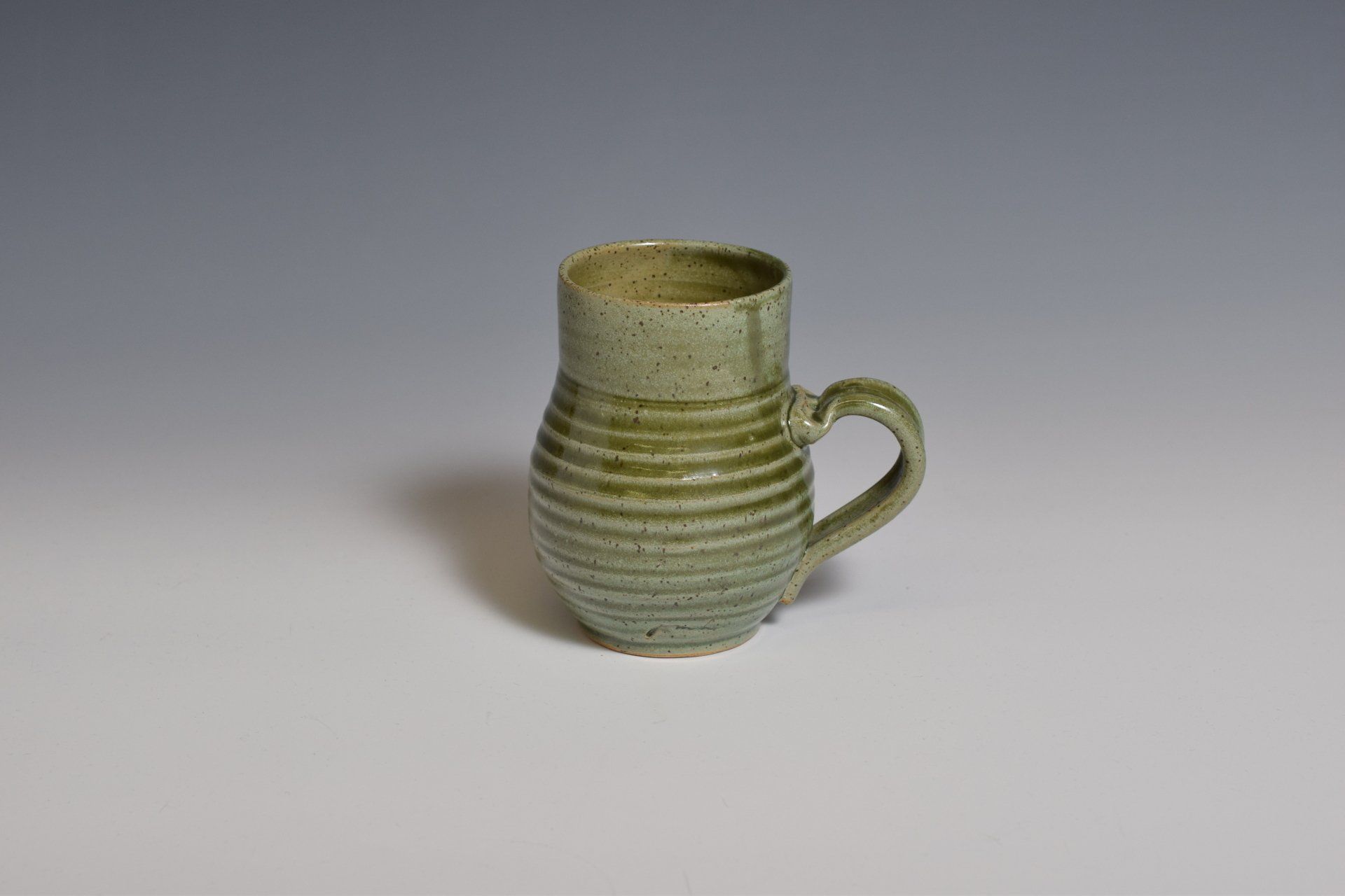 a green mug with a handle is sitting on a white table .